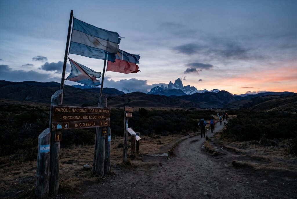Patagonia trailhead at dawn with hikers, flags, and mountains in the distance